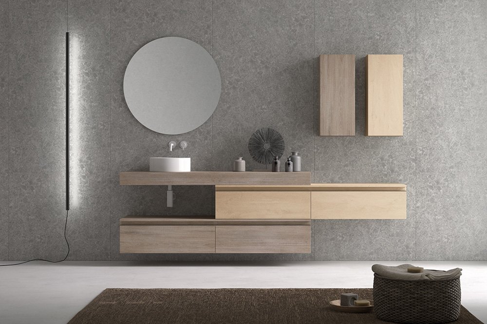 Pared de un aseo de estilo moderno en donde se ve un espejo redondo y un mueble con un pequeño lavabo y cuatro cajone