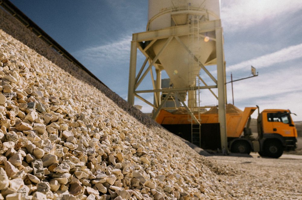 Vista en primer plano de un montón de gravilla y al fondo un camión volquete