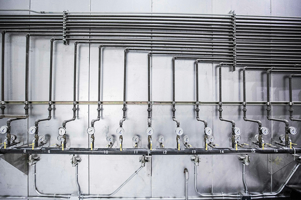 Pared de cemento con una serie de tuberías que desembocan en medidores de caudal hacia una tubería principal