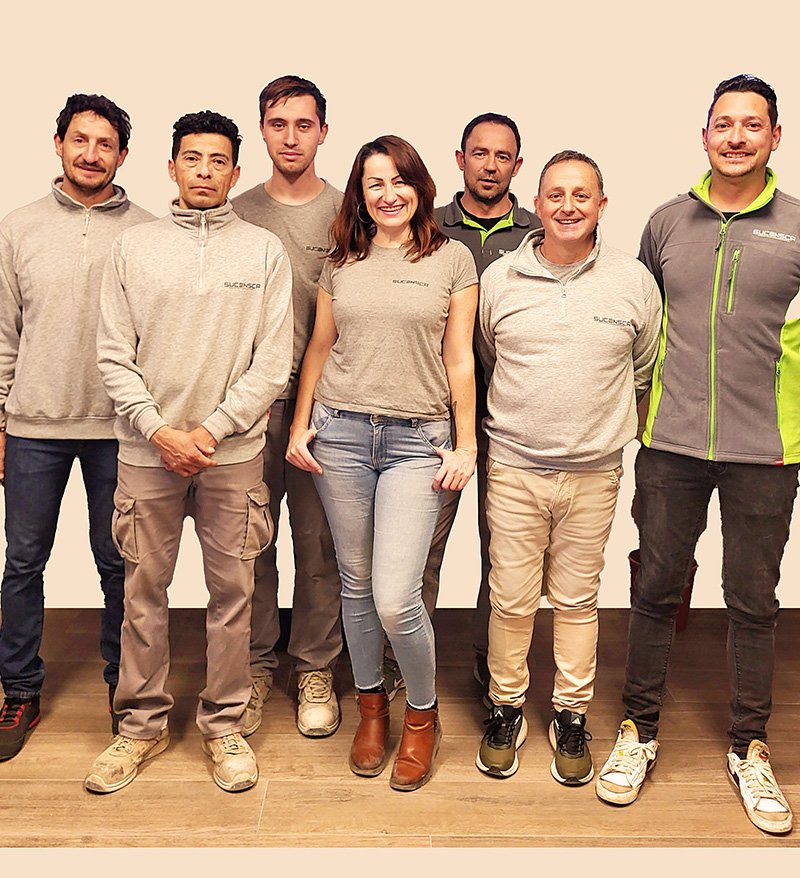 Grupo de seis hombre y una mujer con ropa de trabajo posando y sonriendo