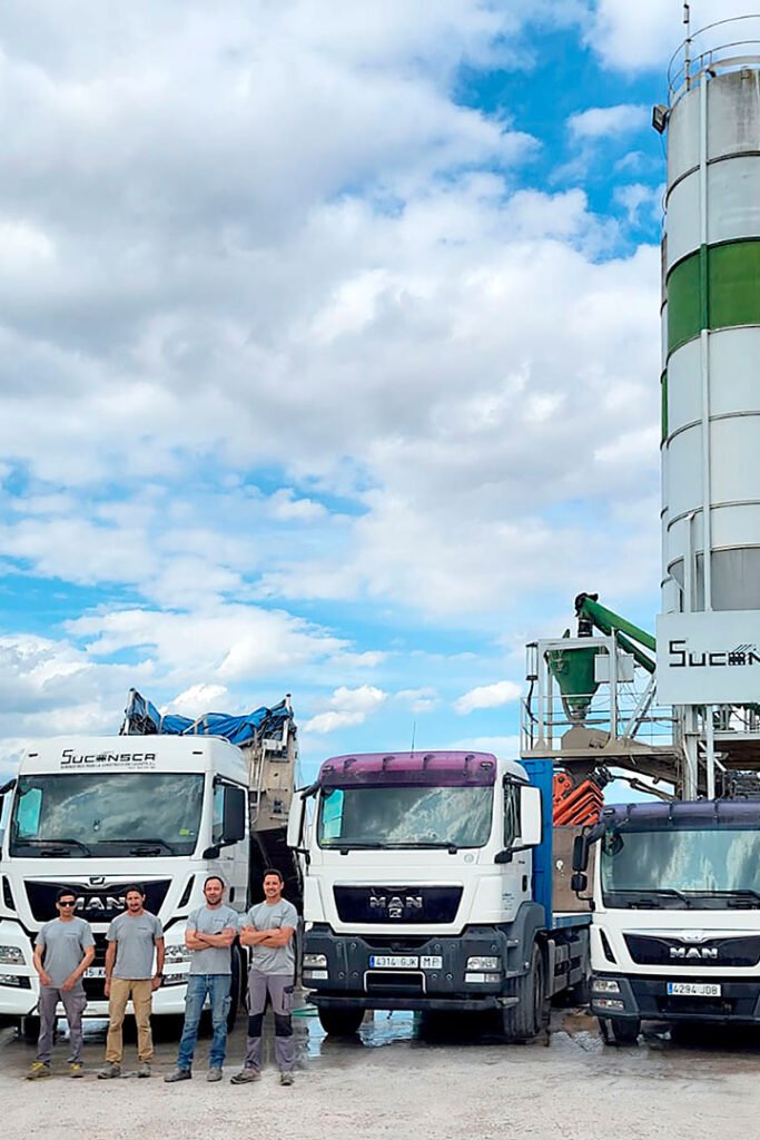 Foto de planta de hormigón de Suconsca con varios vehículos aparcados delante y un grupo de cuatro trabajadores