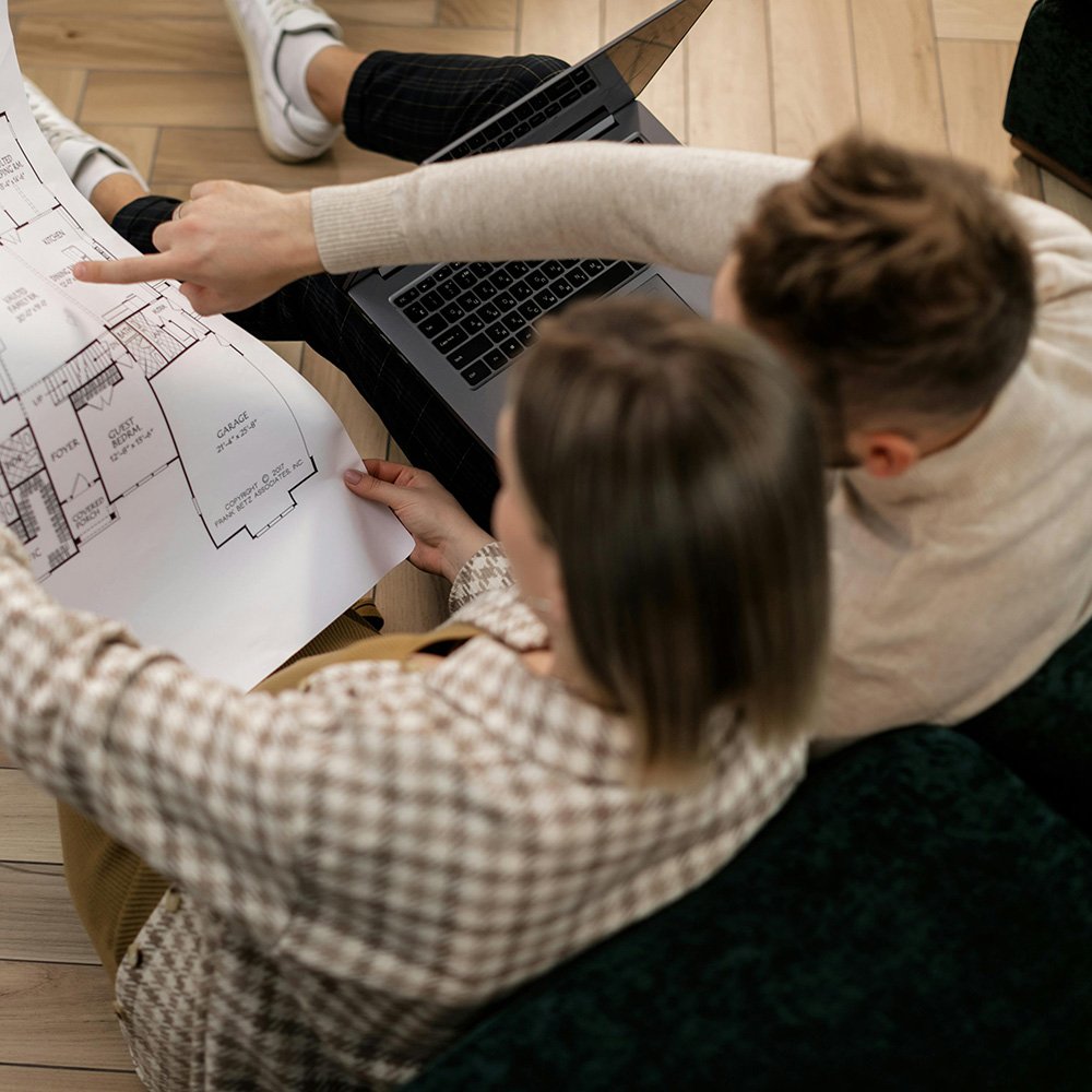 Una pareja sentada en un sofá, vista desde arriba, consultando un plano de construcción.