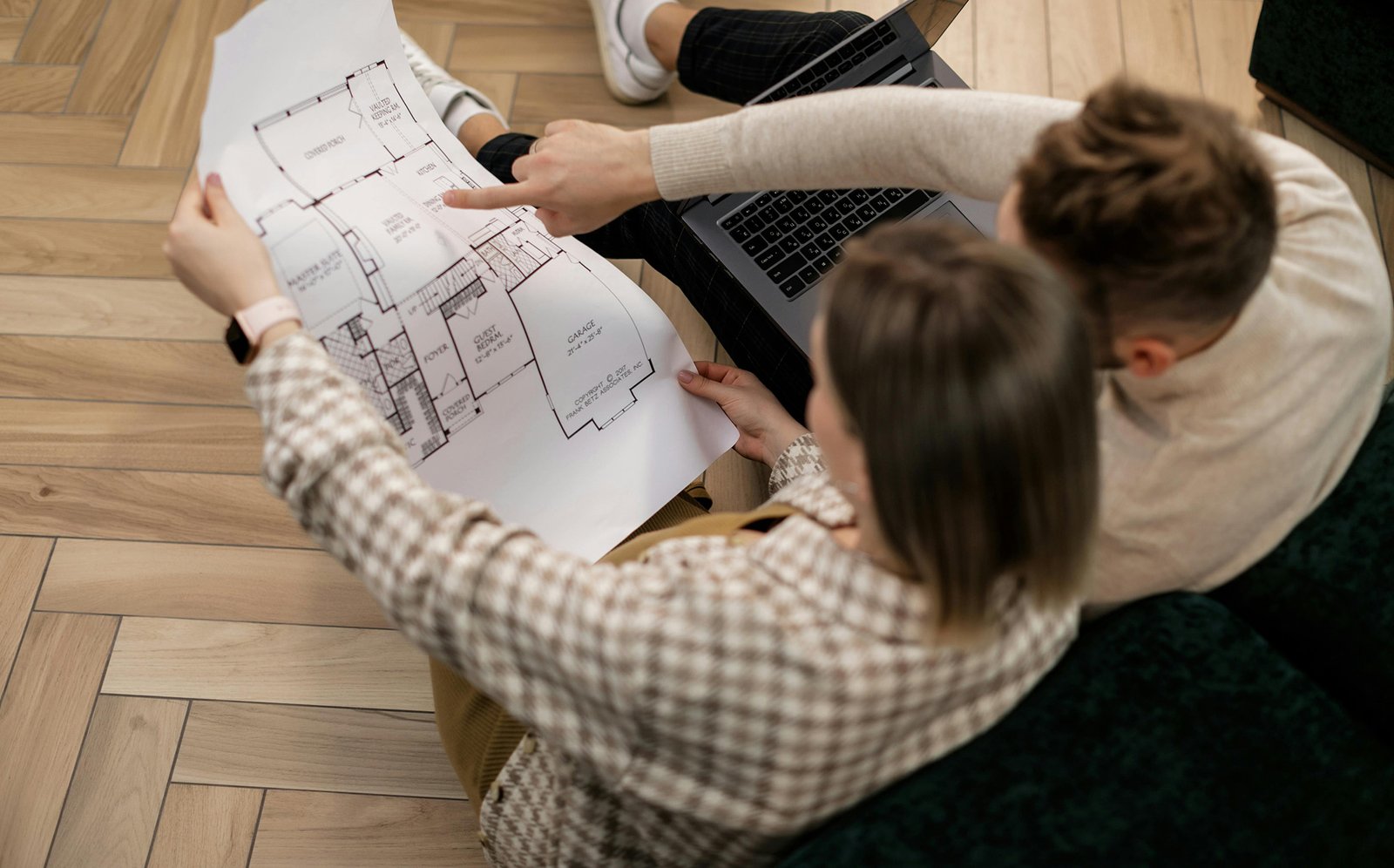 Dos personas sentadas consultando un plano y un ordenador portátil, vistos desde arriba